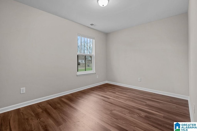 spare room featuring dark wood finished floors, visible vents, and baseboards