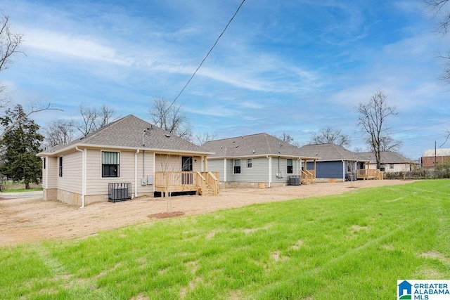 rear view of property featuring a shingled roof, a lawn, a wooden deck, and central AC unit