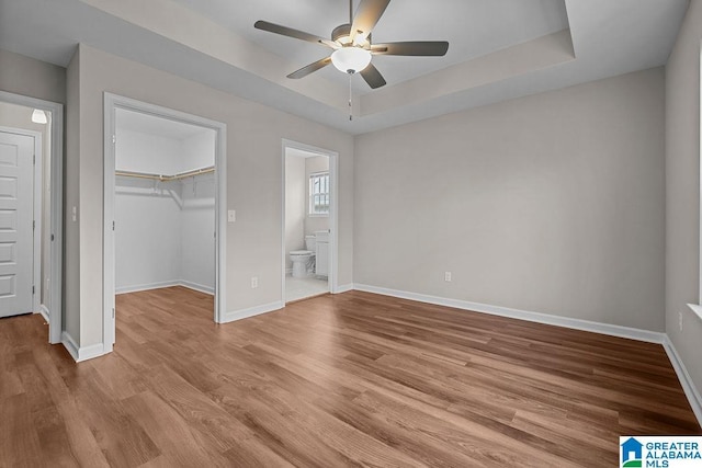 unfurnished bedroom with light wood-style floors, a raised ceiling, a closet, and baseboards