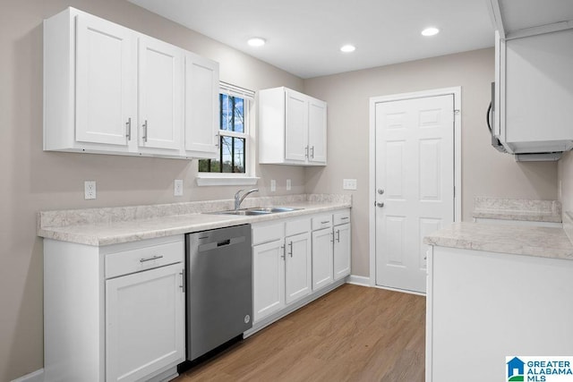 kitchen featuring light countertops, light wood-type flooring, stainless steel dishwasher, white cabinetry, and a sink