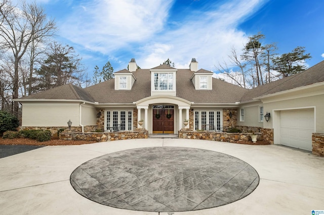 view of front of house with stone siding, a chimney, concrete driveway, and french doors