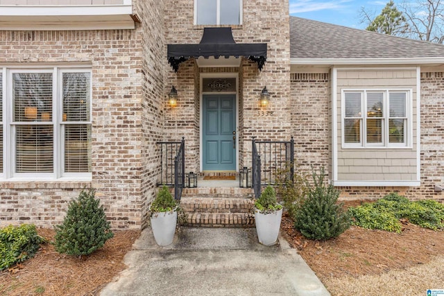 doorway to property featuring brick siding and roof with shingles