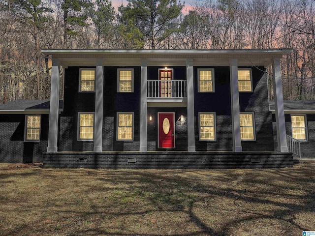 view of front of house featuring a balcony, a lawn, and brick siding