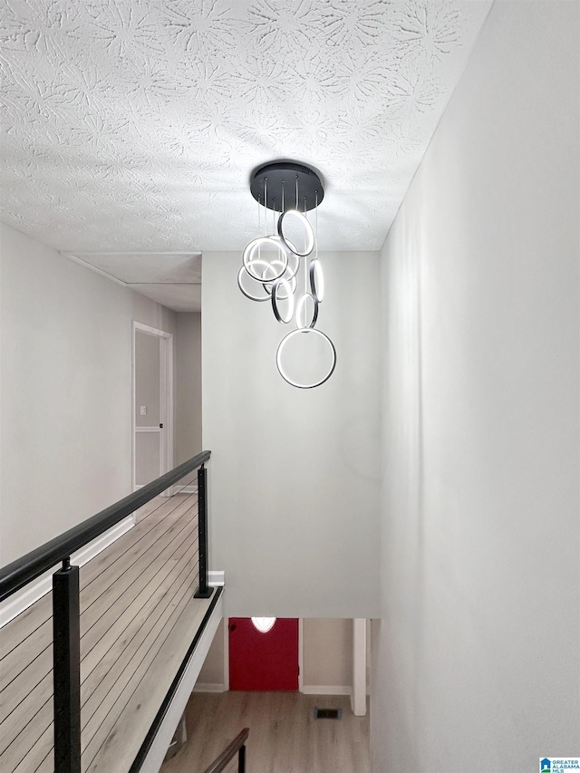 stairs with a notable chandelier, a textured ceiling, baseboards, and wood finished floors