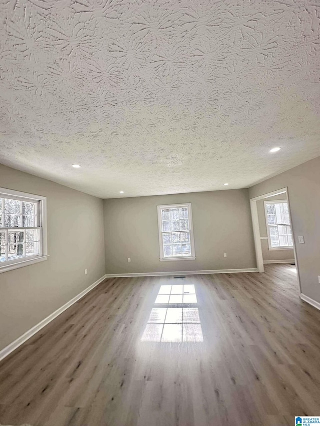 empty room featuring a textured ceiling, recessed lighting, wood finished floors, and baseboards