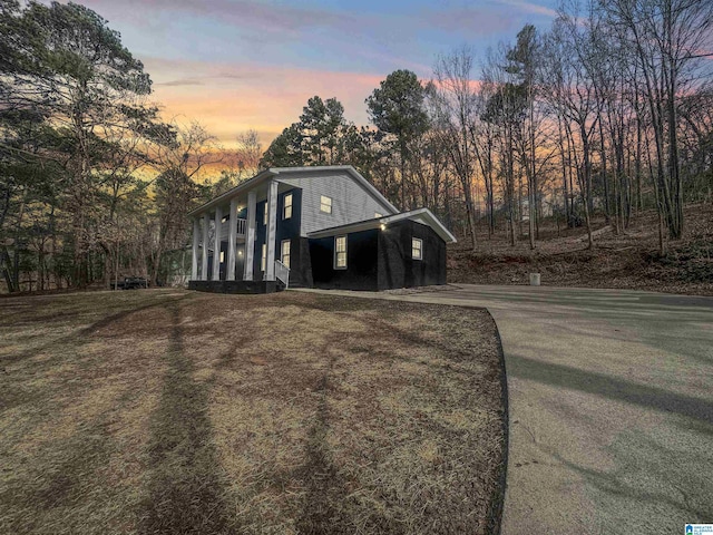 property exterior at dusk with covered porch, driveway, and a lawn