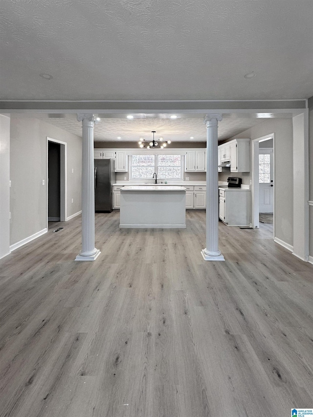 unfurnished living room featuring light wood-style floors, decorative columns, baseboards, and a textured ceiling