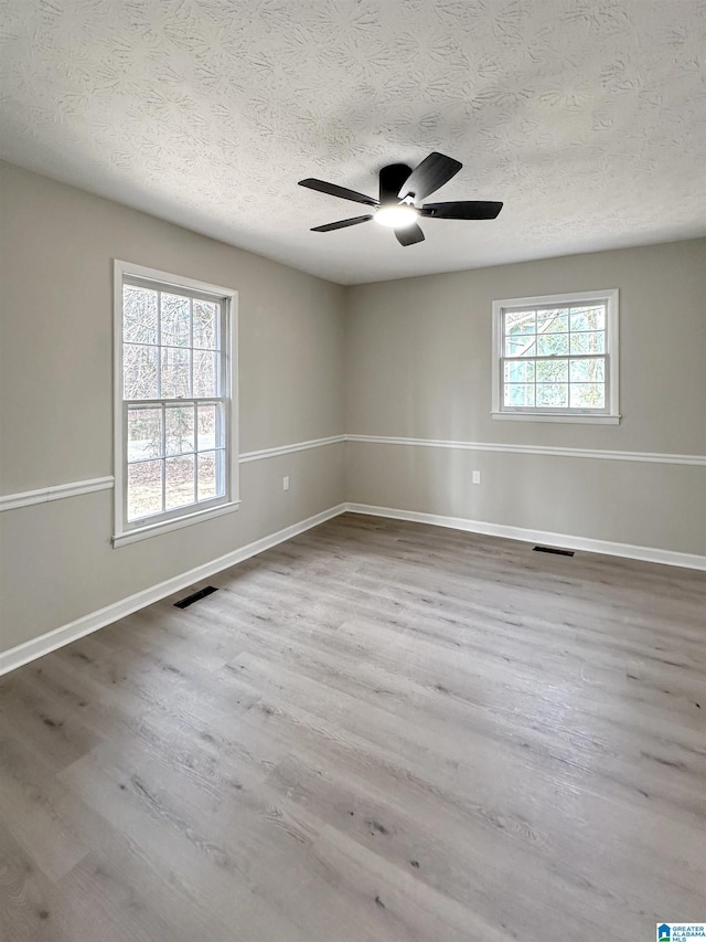 spare room with visible vents, a textured ceiling, baseboards, and wood finished floors