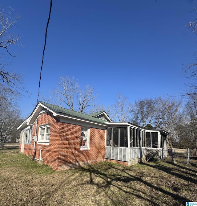 view of home's exterior with metal roof, brick siding, fence, a sunroom, and a yard