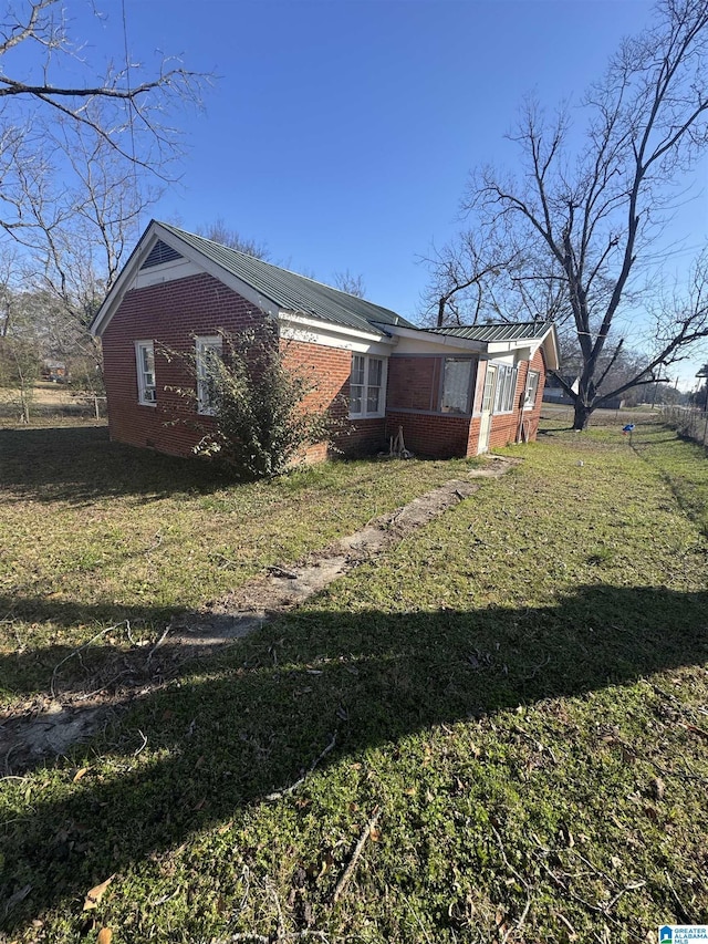 view of side of home featuring metal roof, brick siding, and a yard