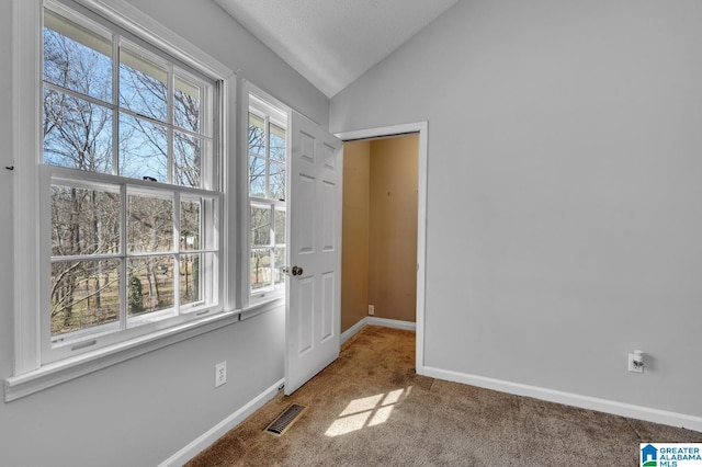 empty room with lofted ceiling, carpet, visible vents, and baseboards