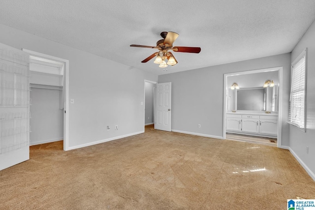 unfurnished bedroom with a spacious closet, light carpet, a textured ceiling, ensuite bath, and baseboards