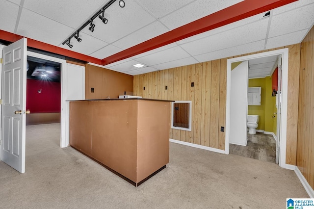 kitchen with a paneled ceiling, wood walls, track lighting, and light colored carpet