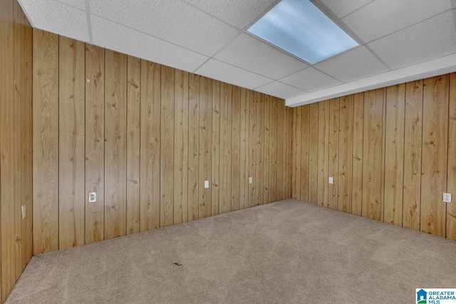 carpeted spare room featuring a drop ceiling and wood walls