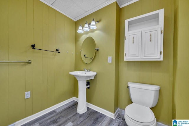 half bath featuring baseboards, toilet, wood finished floors, crown molding, and a sink