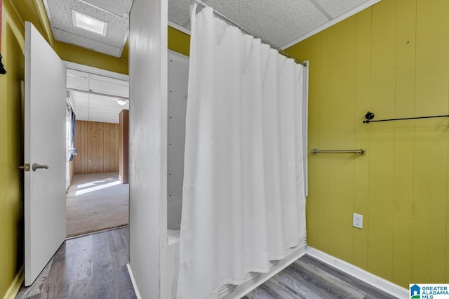 bathroom featuring wood walls, a drop ceiling, and wood finished floors