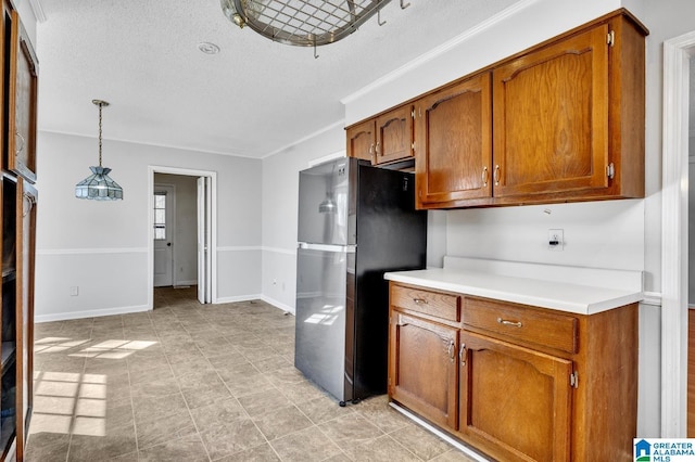 kitchen featuring baseboards, hanging light fixtures, light countertops, freestanding refrigerator, and brown cabinets