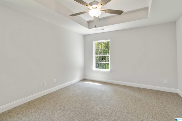 carpeted empty room featuring baseboards, visible vents, a raised ceiling, and a ceiling fan