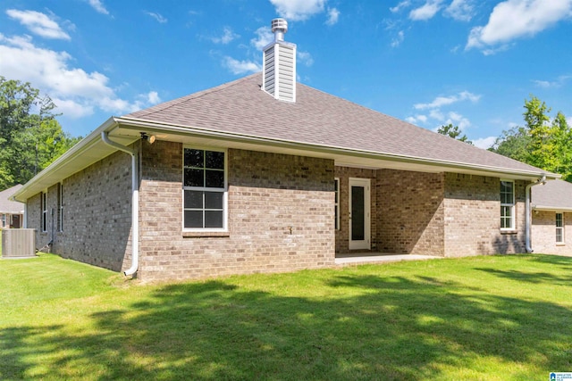 rear view of property with brick siding, a chimney, cooling unit, and a yard