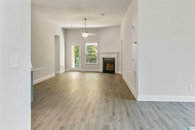 unfurnished living room with light wood finished floors, a fireplace with flush hearth, baseboards, and a ceiling fan