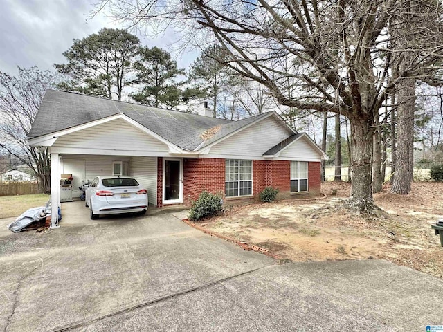 ranch-style home with concrete driveway, a chimney, an attached carport, roof with shingles, and brick siding