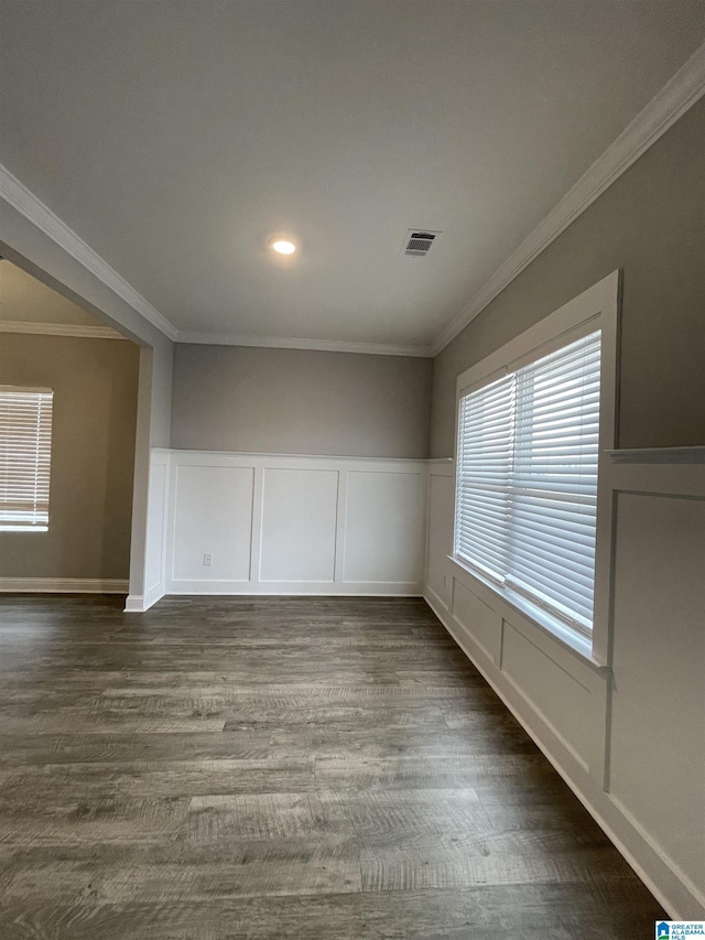 empty room featuring visible vents, dark wood-type flooring, ornamental molding, and a decorative wall