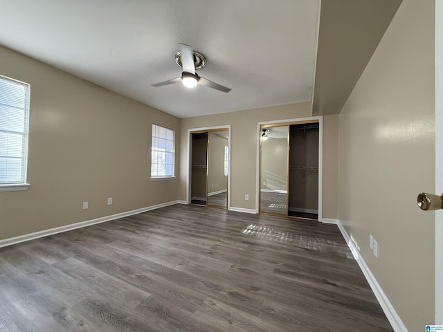 unfurnished bedroom with ceiling fan, baseboards, two closets, and wood finished floors