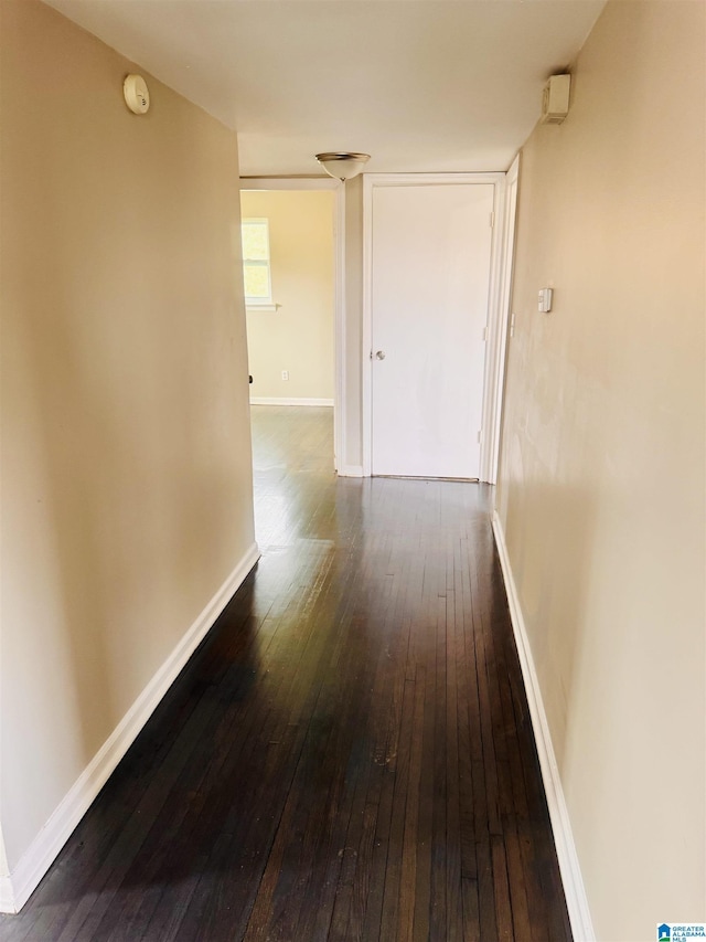 hallway featuring dark wood-style flooring and baseboards