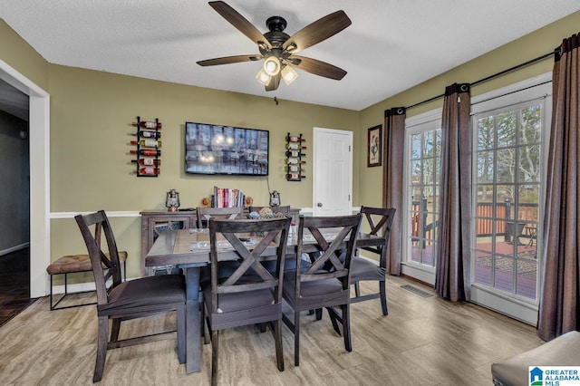 dining area featuring light wood finished floors, ceiling fan, visible vents, and a textured ceiling