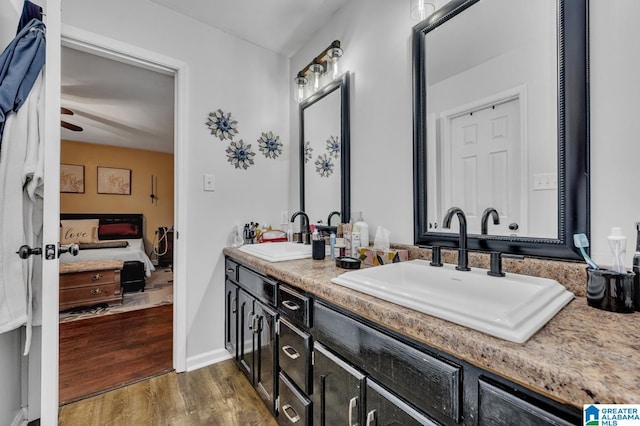 ensuite bathroom featuring double vanity, a sink, ensuite bath, and wood finished floors