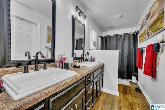 full bath featuring double vanity, wood finished floors, a sink, and visible vents