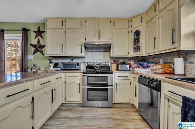 kitchen with under cabinet range hood, cream cabinets, appliances with stainless steel finishes, and light countertops