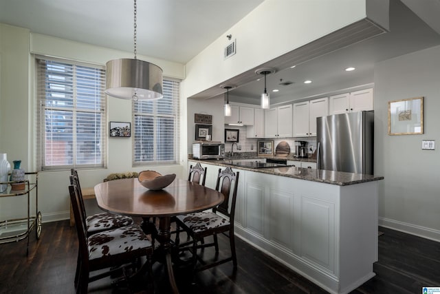 kitchen with visible vents, white cabinetry, freestanding refrigerator, dark stone countertops, and decorative light fixtures