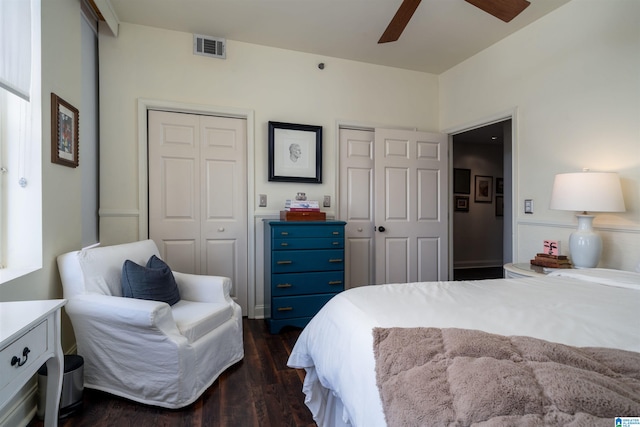 bedroom featuring dark wood-type flooring, two closets, visible vents, and a ceiling fan