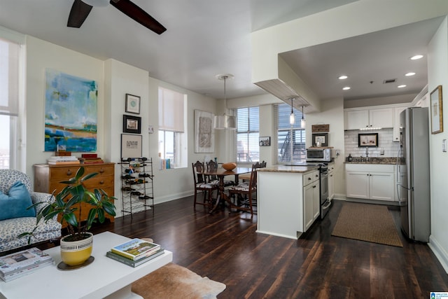 kitchen featuring white cabinets, dark wood finished floors, a peninsula, stainless steel appliances, and pendant lighting