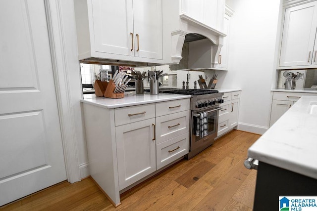 kitchen featuring light stone counters, high end stainless steel range, white cabinetry, and light wood-style floors