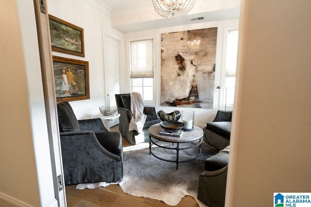 living area featuring ornamental molding, wood finished floors, visible vents, and an inviting chandelier