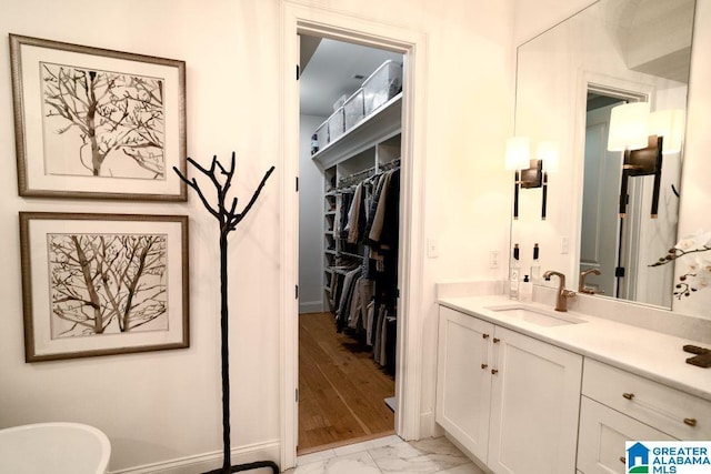 full bathroom featuring marble finish floor, a freestanding tub, a walk in closet, and vanity