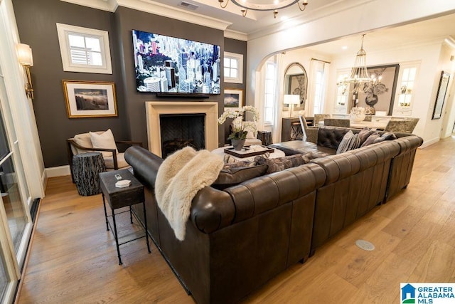 living room with light wood-style floors, a fireplace, arched walkways, and crown molding