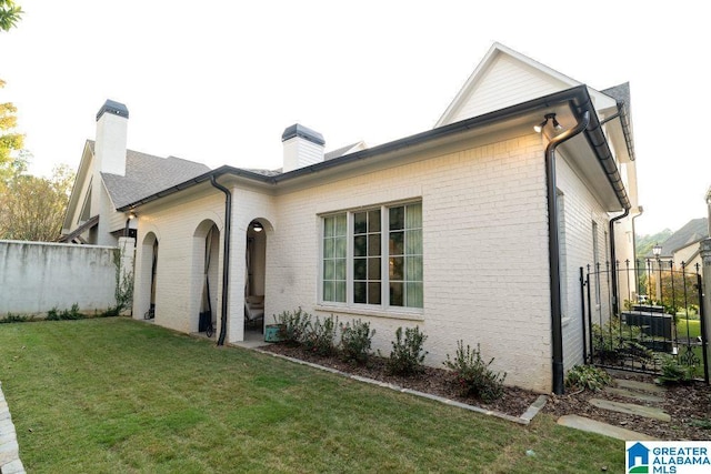 rear view of house featuring a yard, brick siding, a chimney, and fence