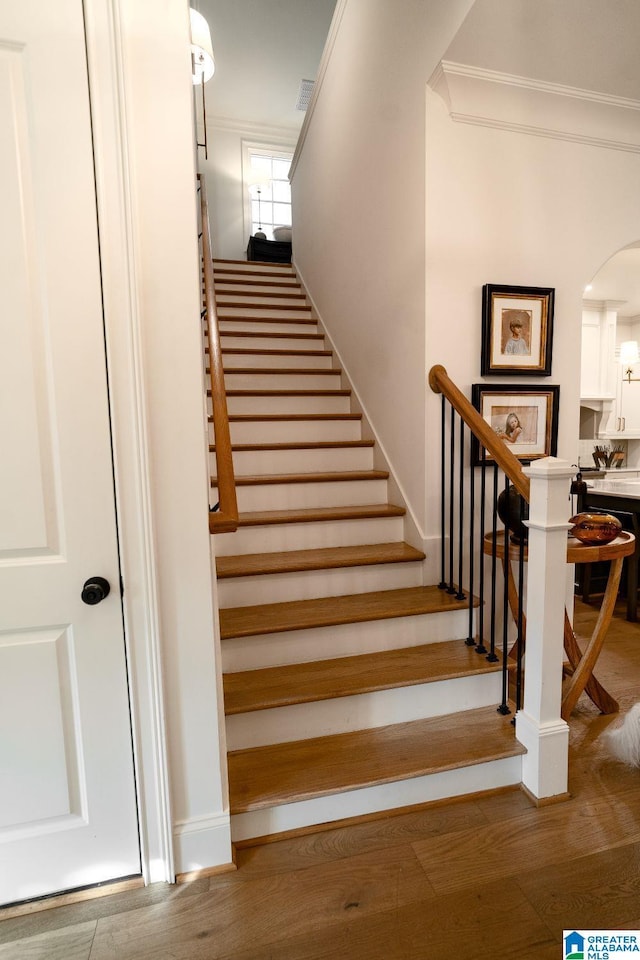 staircase with ornamental molding, arched walkways, visible vents, and wood finished floors