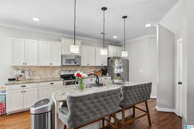 kitchen featuring a center island with sink, white cabinets, decorative light fixtures, stainless steel appliances, and a kitchen bar