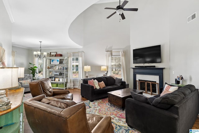 living room with crown molding, a fireplace, visible vents, wood finished floors, and ceiling fan with notable chandelier