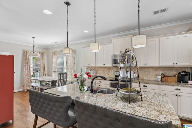 kitchen featuring a kitchen island with sink, stainless steel appliances, visible vents, ornamental molding, and pendant lighting