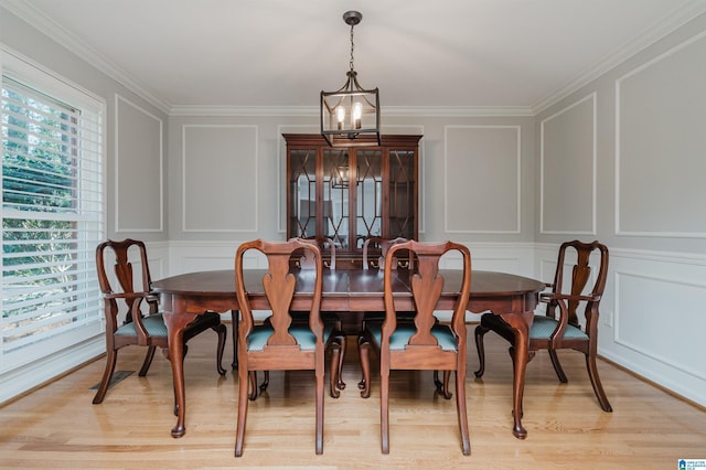 dining area with light wood-style flooring, crown molding, a decorative wall, and a notable chandelier