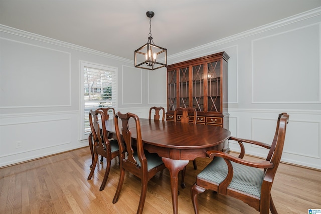 dining space featuring light wood-type flooring, a chandelier, a decorative wall, and crown molding