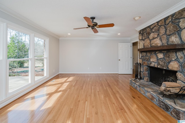 living room featuring light wood-style flooring, crown molding, a stone fireplace, and baseboards