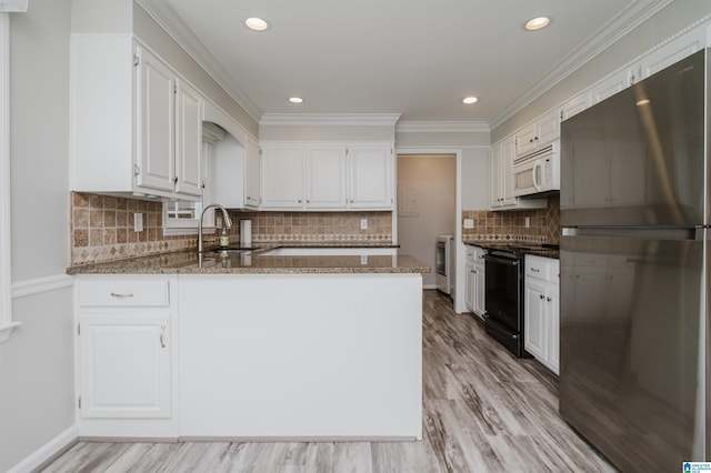 kitchen featuring electric stove, white microwave, freestanding refrigerator, white cabinets, and dark stone countertops