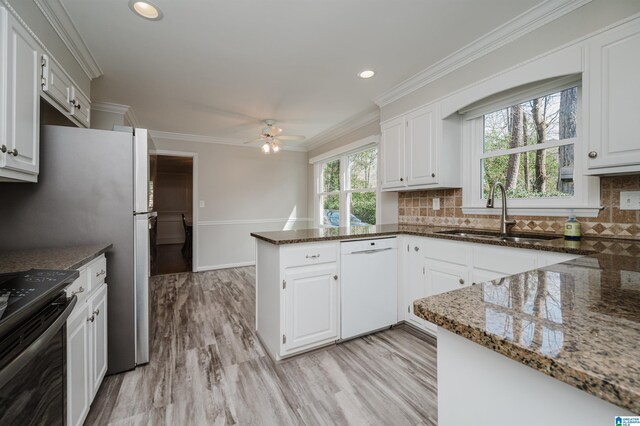 kitchen featuring white cabinets, a sink, dark stone counters, dishwasher, and a peninsula