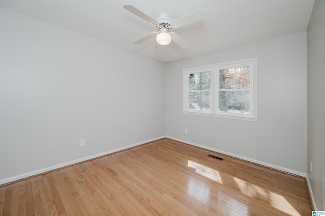 empty room with light wood finished floors, a ceiling fan, visible vents, and baseboards